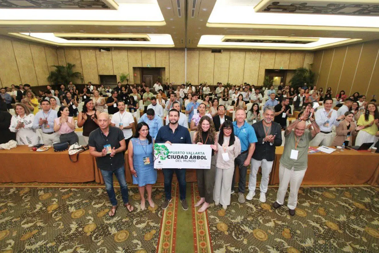A group of diverse individuals stands together in a room, with a prominent green sign visible in the background.