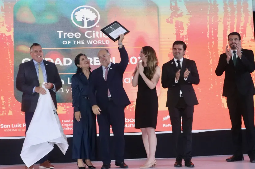 Group of formally dressed people on stage celebrating a Tree Cities of the World award presentation.