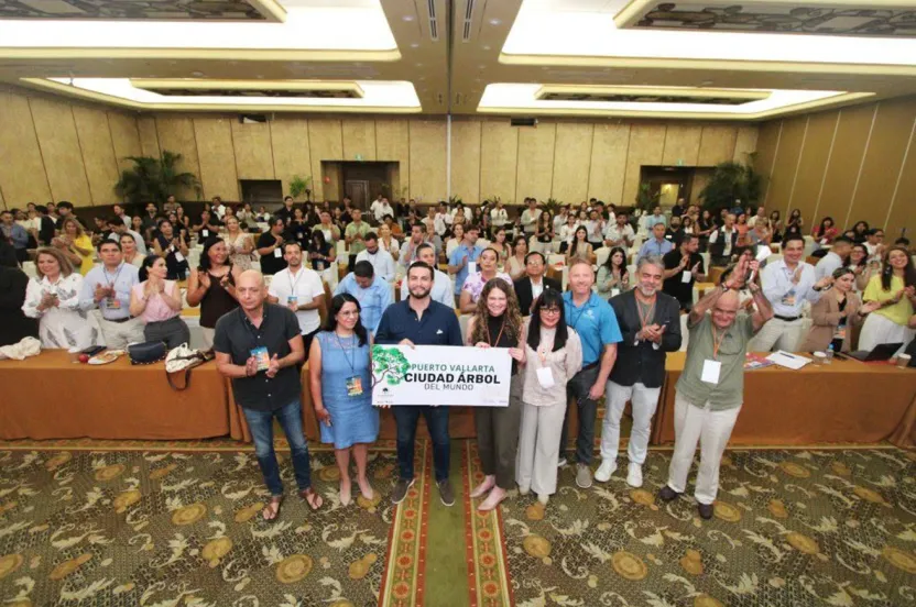 A group of diverse individuals stands together in a room, with a prominent green sign visible in the background.